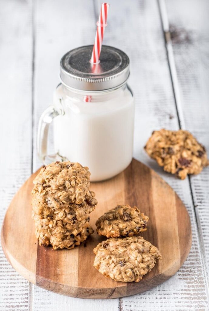 a glass jar with a straw next to cookies and a glass of milk