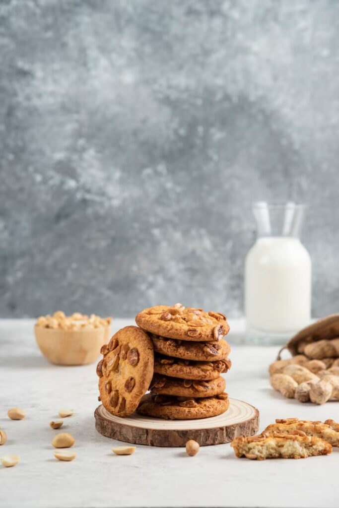 a stack of cookies with peanuts in a bowl and a glass of milk