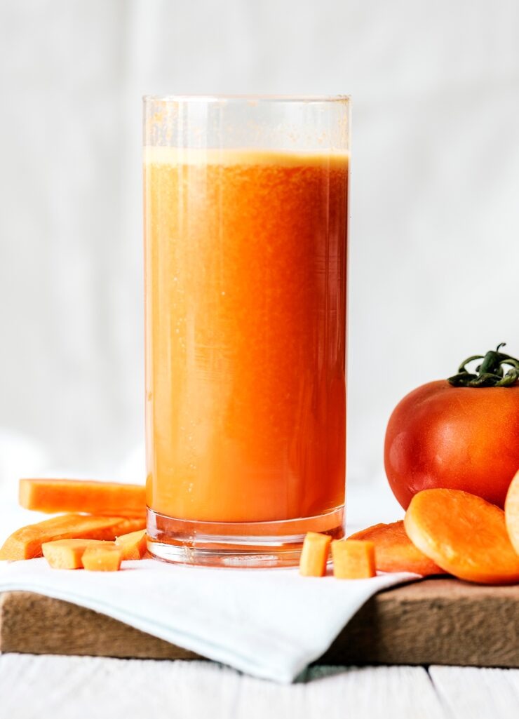 a glass of carrot juice next to a tomato