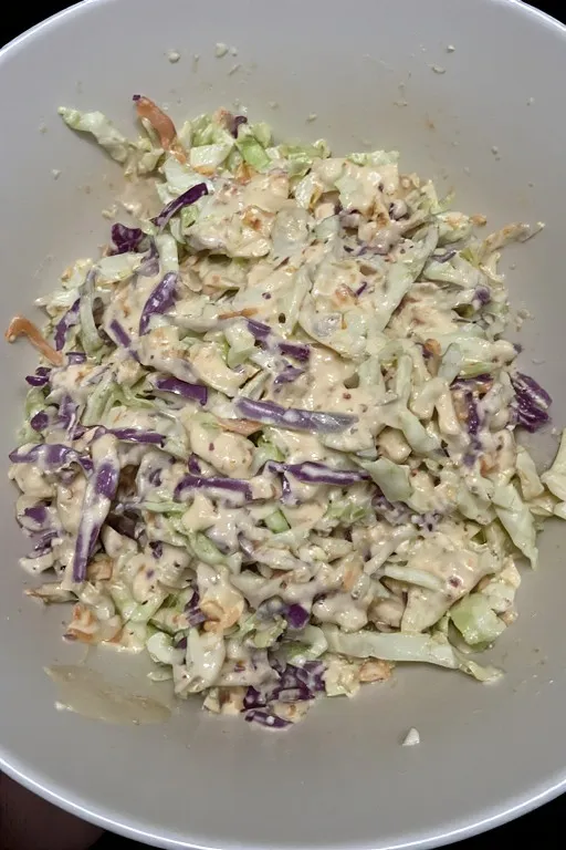 pouring creamy dressing over coleslaw and tossing