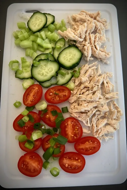Prepped ingredients for chicken pasta salad including shredded chicken and fresh vegetables.
