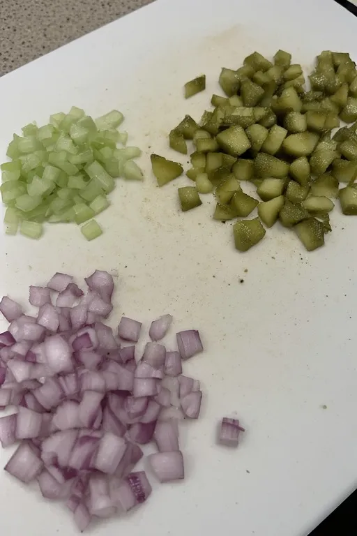 Diced dill pickles and vegetables prepped on cutting board for pickle pasta salad