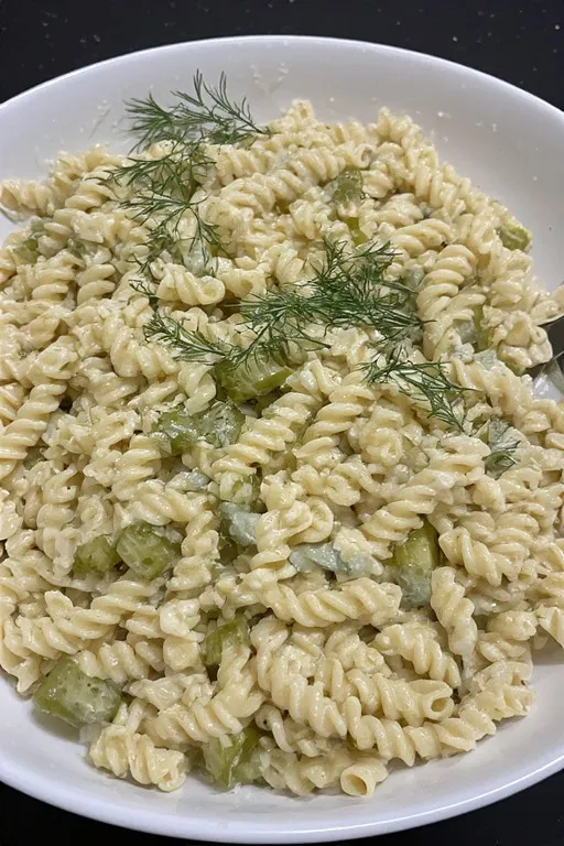  Creamy dill pickle pasta salad being tossed with dressing in a large bowl