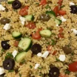 Alt text: Finished orzo pasta salad in a serving bowl with feta and fresh herbs in a bowl.