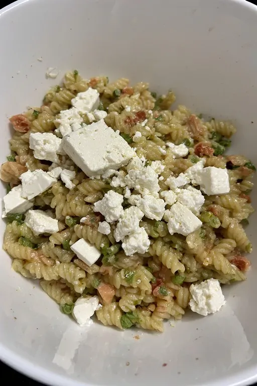 " Alt text: Crumbled feta being folded into fresh orzo pasta salad