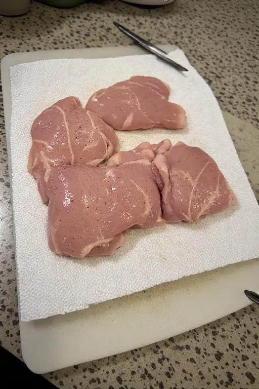 Boneless skinless chicken thighs being patted dry for crispy air fryer chicken thighs recipe