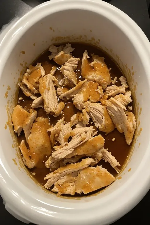 Crockpot chicken thighs being shredded with forks showing fall-apart tender texture