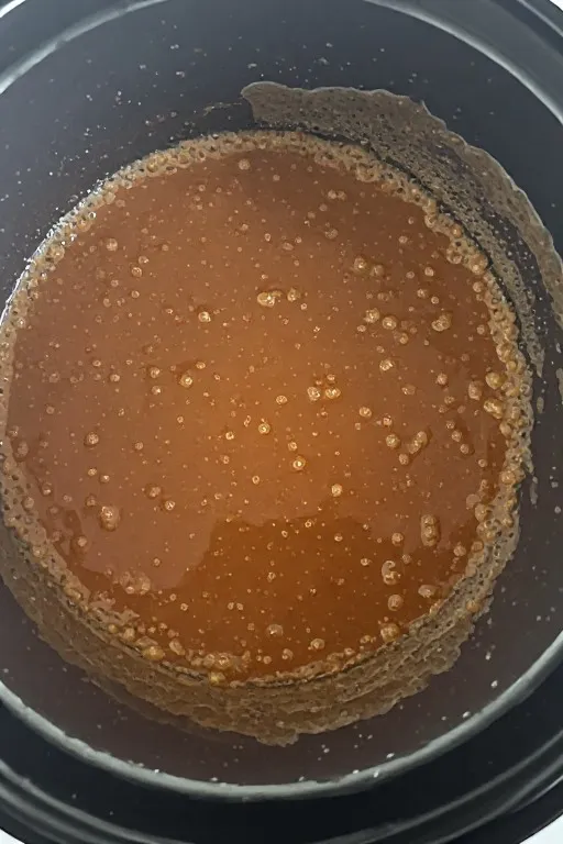 Crockpot chicken thighs cooking liquid being reduced into glossy sauce on stovetop