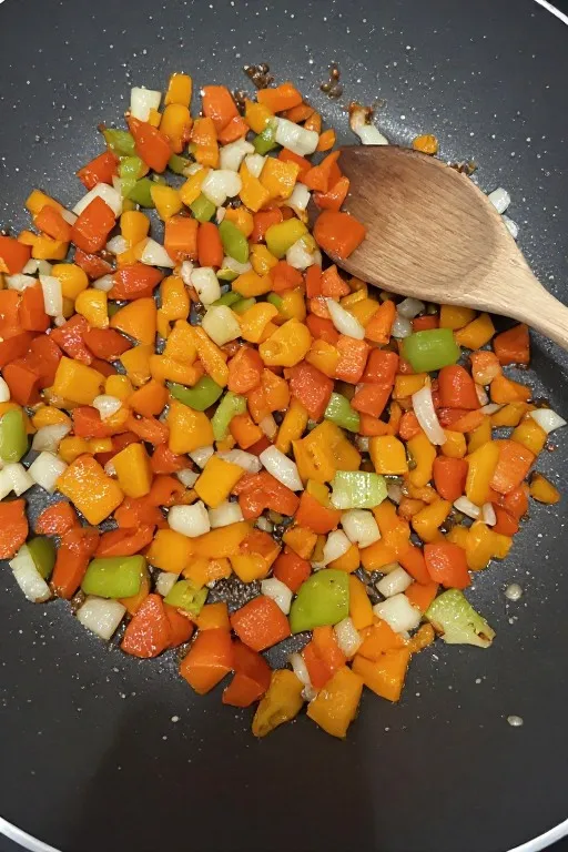 Bell peppers and onion sautéing in skillet for freezer breakfast burrito filling