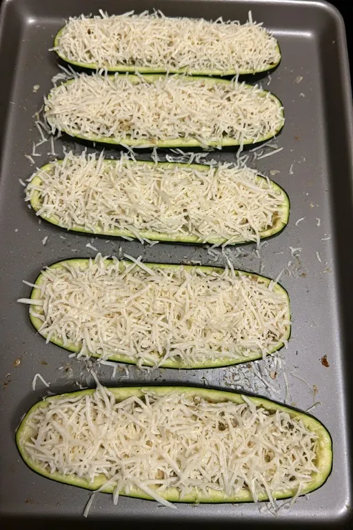 Keto zucchini boats topped with mozzarella and Parmesan ready to bake