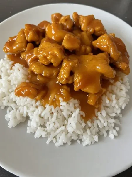 Crock pot apricot chicken plated over rice with thick glossy sauce and parsley