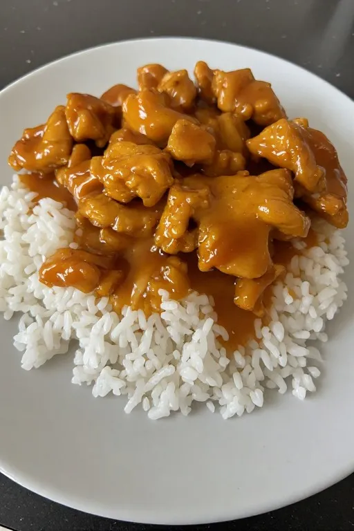 Crock pot apricot chicken plated over rice with thick glossy sauce and parsley