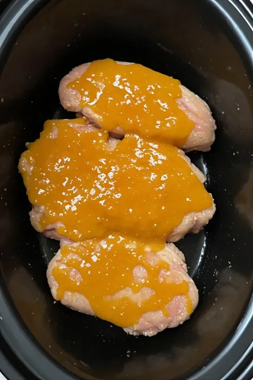 Raw chicken thighs with apricot sauce in slow cooker before cooking