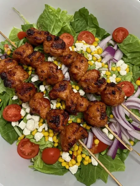 BBQ chicken skewer salad with romaine, corn, cotija and cherry tomatoes in a bowl