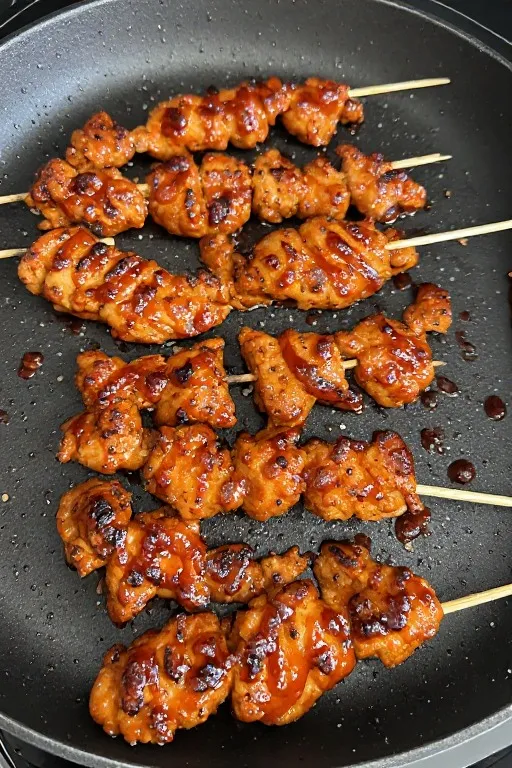 BBQ chicken skewers cooking on grill pan with caramelized sauce and char marks