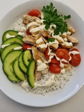 Finished chicken rice bowl with creamy garlic sauce, avocado and fresh vegetables ready to eat