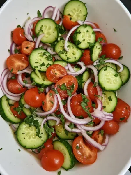 Cucumber tomato onion salad in white bowl with fresh herbs and vinegar dressing