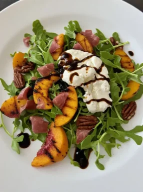 Grilled peach salad with burrata prosciutto arugula and balsamic honey dressing on plate