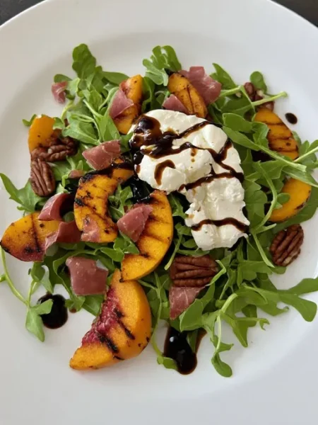 Grilled peach salad with burrata prosciutto arugula and balsamic honey dressing on plate