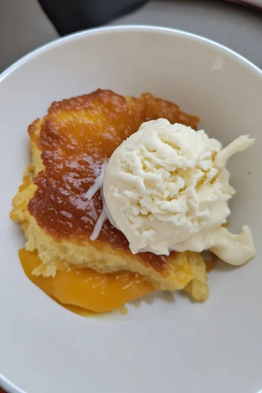 Peach dump cake served in bowl with vanilla ice cream