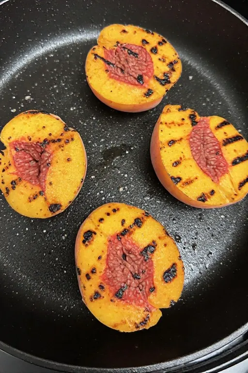 Peach halves grilling on cast iron pan with caramelized grill marks for grilled peach salad