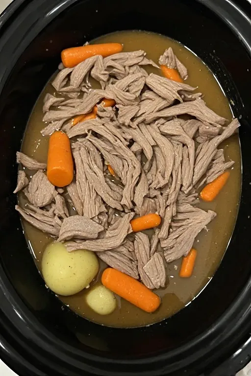 Shredded slow cooker pot roast with tender beef carrots and potatoes in rich broth