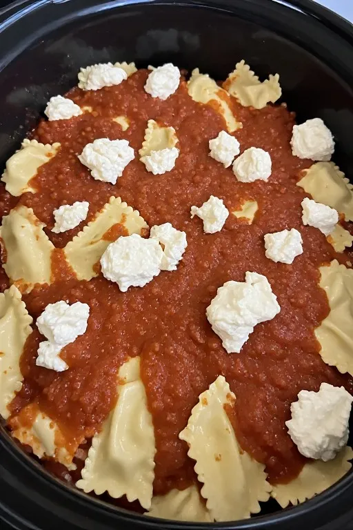 Layering ravioli lasagna in crockpot with marinara and ricotta for crockpot ravioli lasagna recipe