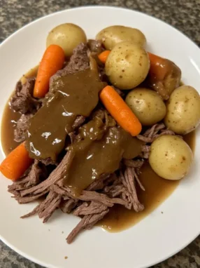 Slow cooker pot roast served in bowl with shredded beef potatoes carrots and gravy