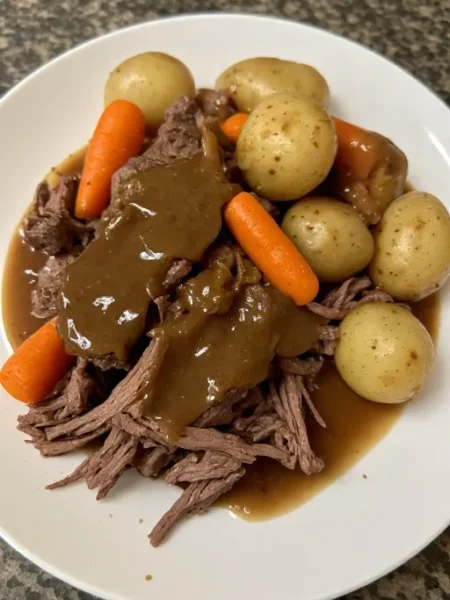 Slow cooker pot roast served in bowl with shredded beef potatoes carrots and gravy