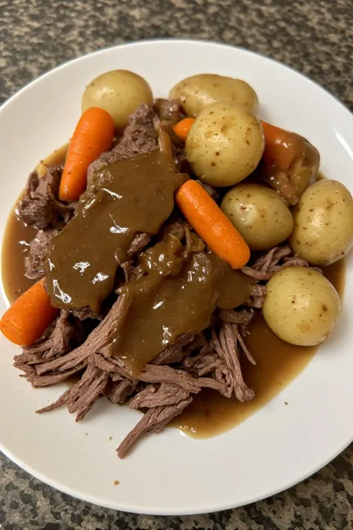 Slow cooker pot roast served in bowl with shredded beef potatoes carrots and gravy