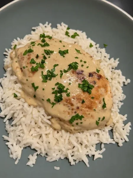 Creamy smothered chicken and rice in a bowl with garlic cream sauce and fresh parsley