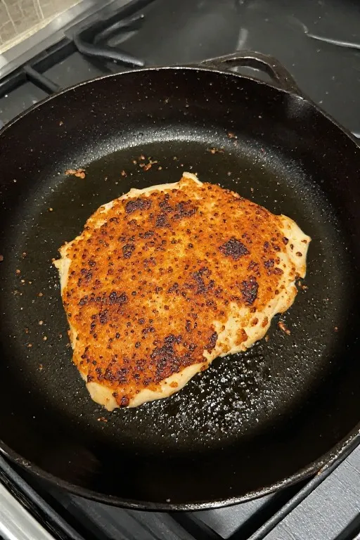 Chicken breast searing in cast iron skillet with golden brown crust for smothered chicken recipe