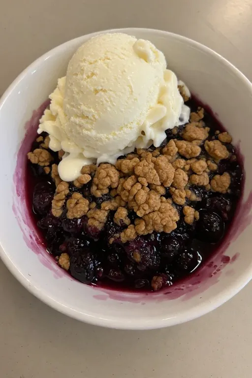 Warm blueberry crisp in bowl topped with melting vanilla ice cream