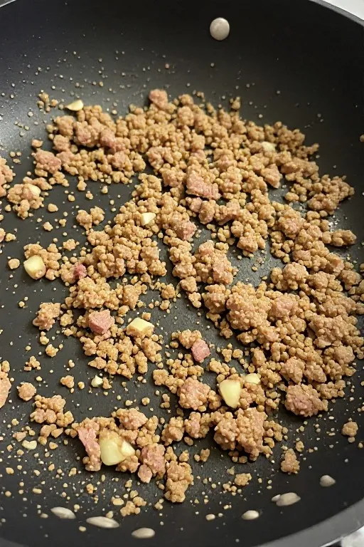 Ground pork browning in skillet with garlic and ginger for egg roll in a bowl recipe