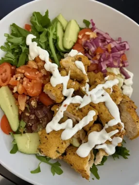 Greek chicken bowl with grilled chicken rice cucumber tomato feta and tzatziki in white bowl