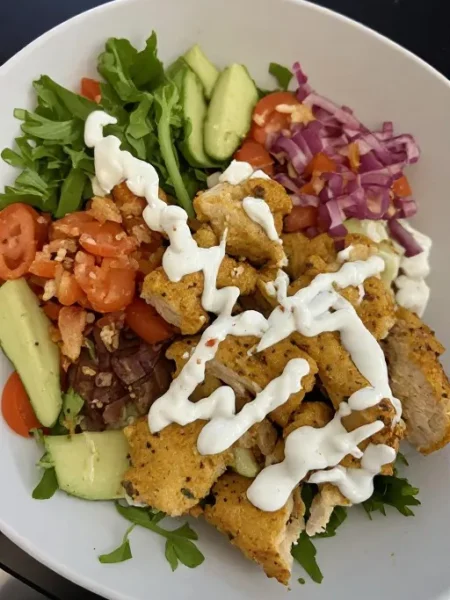 Greek chicken bowl with grilled chicken rice cucumber tomato feta and tzatziki in white bowl