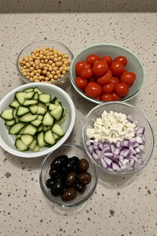Greek chickpea salad ingredients prepped in bowls including chickpeas feta olives and cucumber