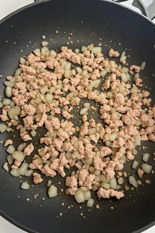 Ground turkey browning with onion and seasoning in skillet