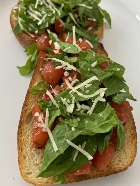 Close up of bruschetta with fresh basil and shaved parmesan on toasted bread