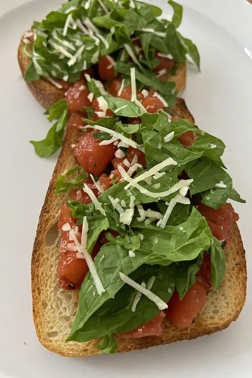 Close up of bruschetta with fresh basil and shaved parmesan on toasted bread