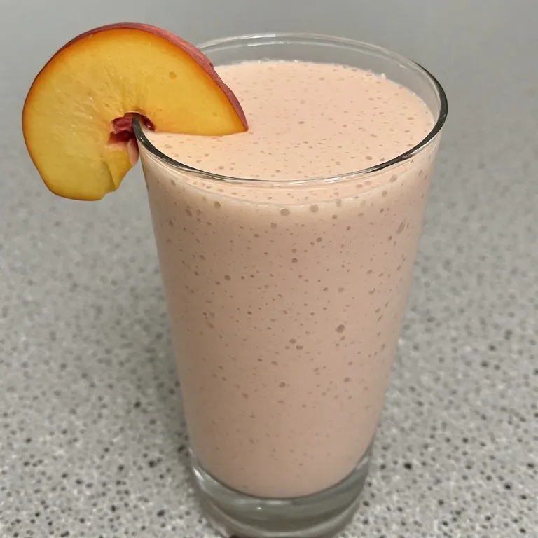 Peach smoothie in tall glass with peach slice garnish