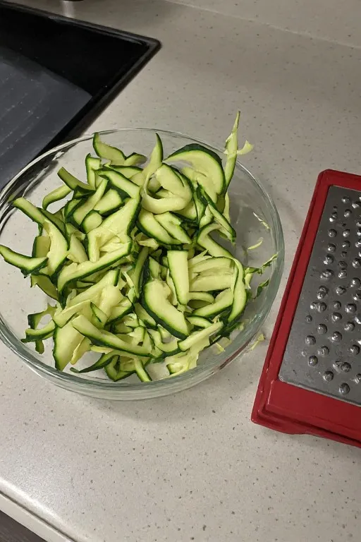Shredded zucchini in bowl beside box grater for zucchini bread recipe