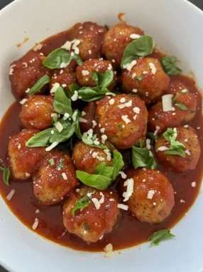 Turkey meatballs in white bowl with marinara sauce and fresh basil