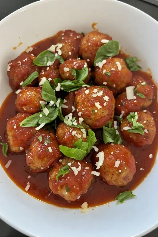Turkey meatballs in white bowl with marinara sauce and fresh basil