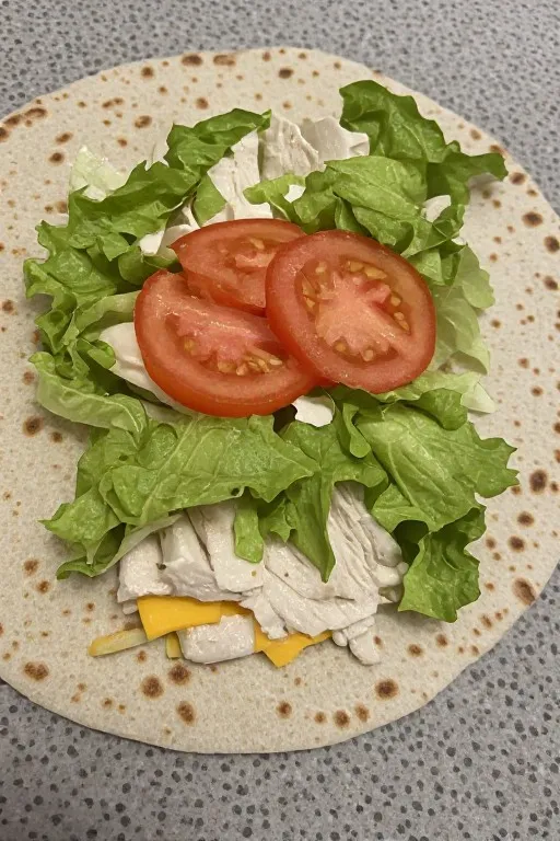 Tortilla with turkey cheese lettuce and tomato layered before rolling