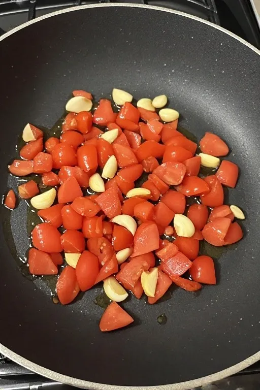 Diced tomatoes and garlic cooking down in skillet with olive oil