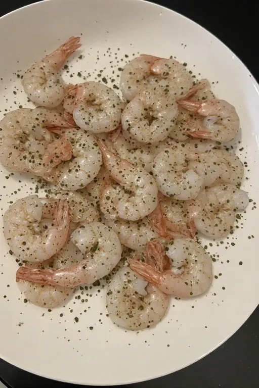 Raw shrimp being seasoned on plate before cooking